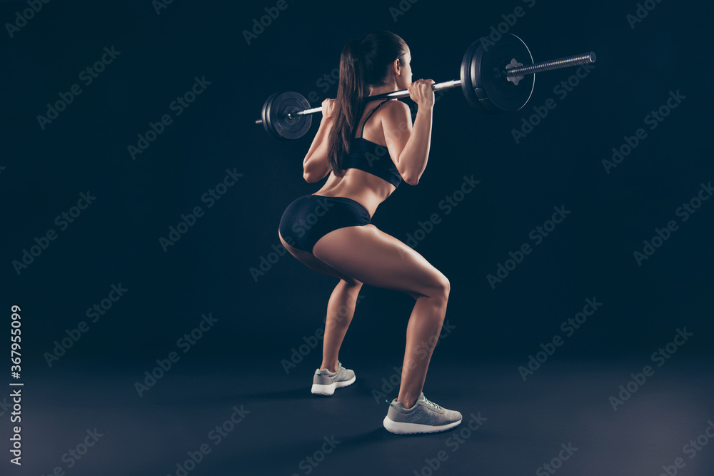 Full body side behind photo active short sport suit lady shoulders heavy barbell fitness doing squats isolated black background