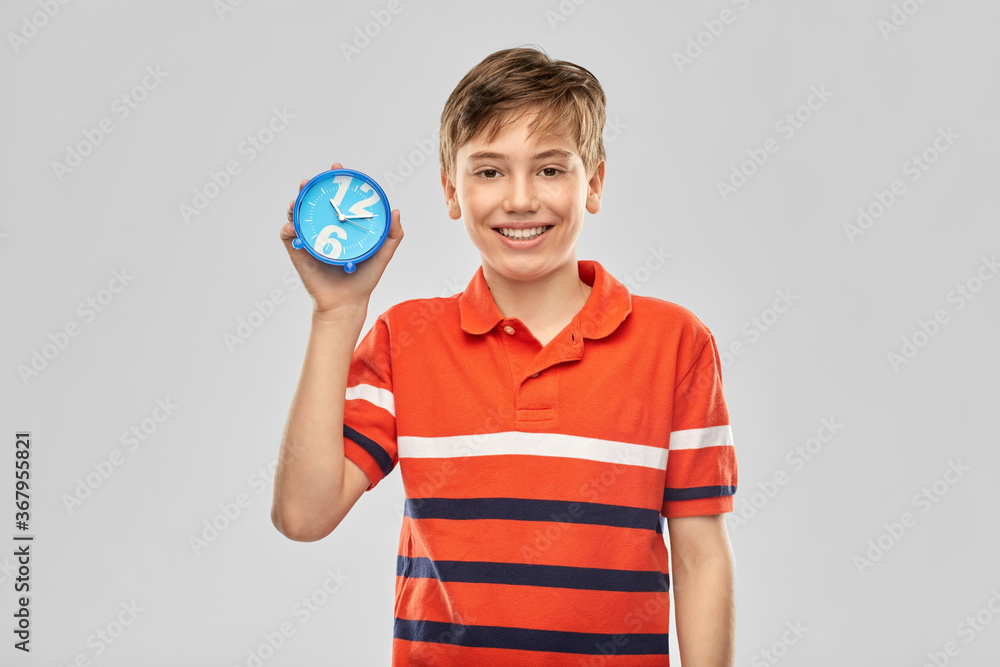 childhood, fashion and people concept - portrait of happy smiling boy in red polo t-shirt with alarm clock over grey background childhood, fashion and people concept - portrait of happy smiling boy in red polo t-shirt with alarm clock over grey background