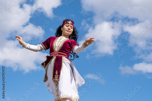 Young tender girl dancing national dance in a beautiful costume under the open blue summer sky