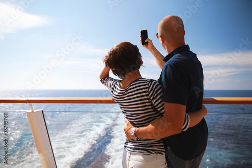 bald man and brunette woman traveling on cruise liner ship and taking pictures from smartphone on balcony 