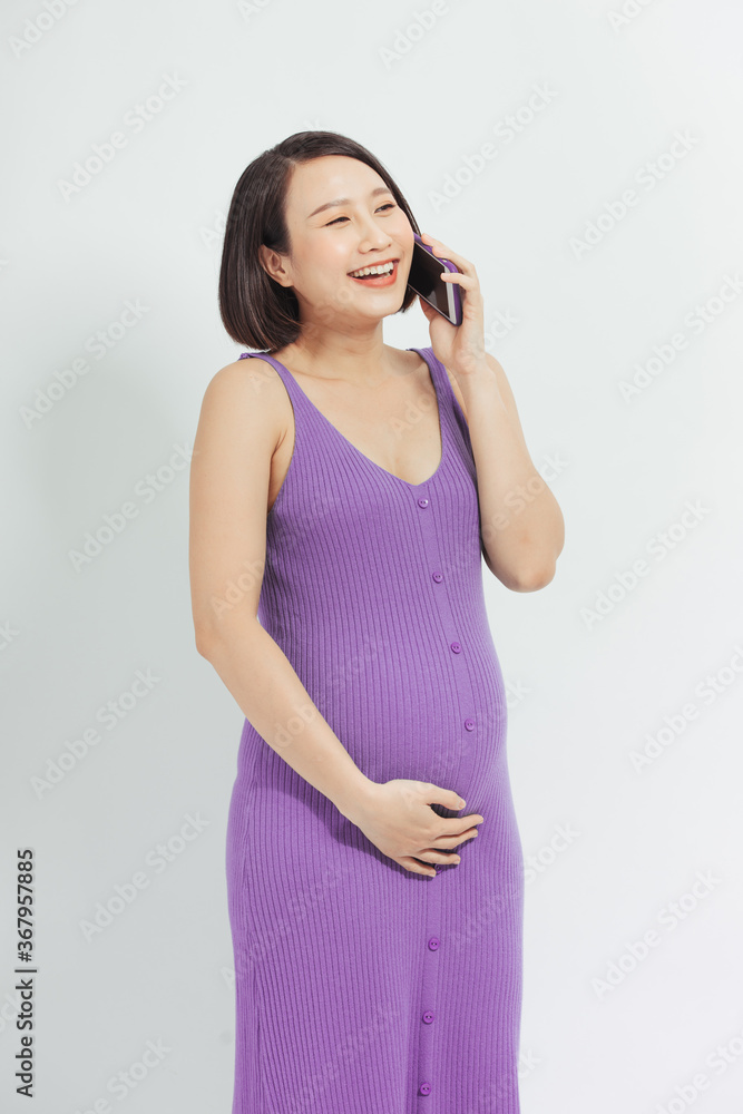 Happy Pregnant Lady Talking On Mobile Phone Touching Belly Standing Over White Studio Background. Free Space Happy Pregnant Lady Talking On Mobile Phone Touching Belly Standing Over White Studio Background. Free Space