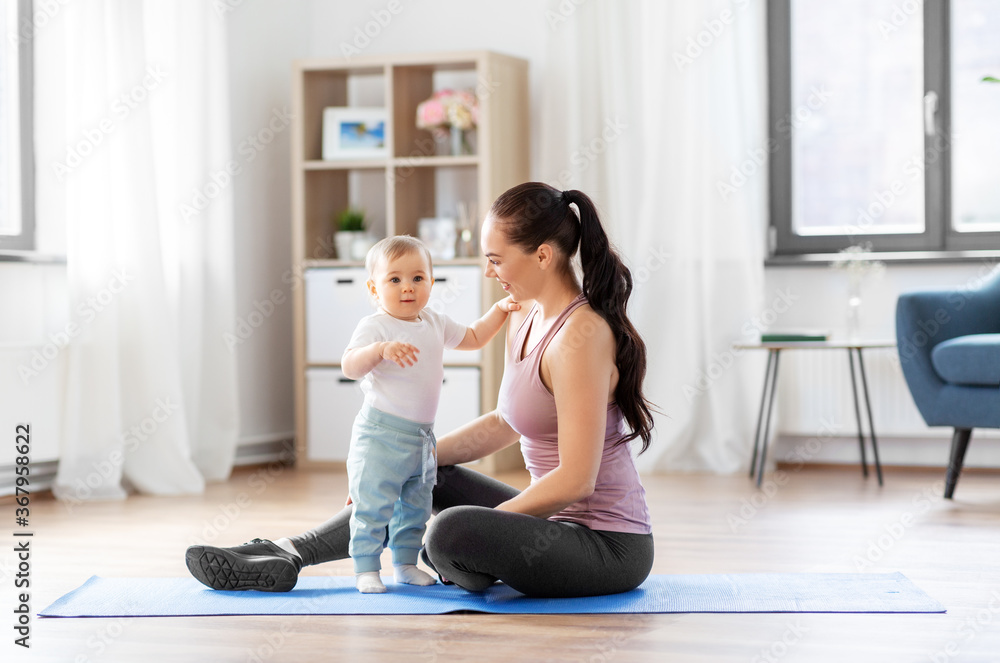 family, sport and motherhood concept - happy smiling mother with little baby sitting on exercise mat at home family, sport and motherhood concept - happy smiling mother with little baby sitting on exercise mat at home