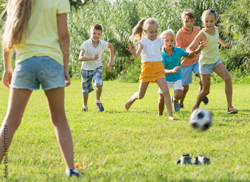 team of energetic joyful children running with ball on meadow outdoors .