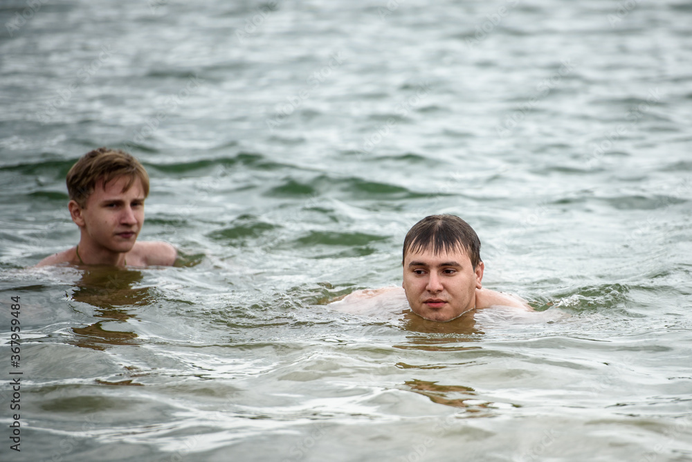 Two guys swim in the lake in the summer in cold weather. The concept of summer vacation Two guys swim in the lake in the summer in cold weather. The concept of summer vacation