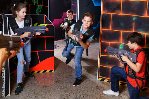 Group of glad friendly teenagers with laser guns having fun on dark lasertag arena © JackF