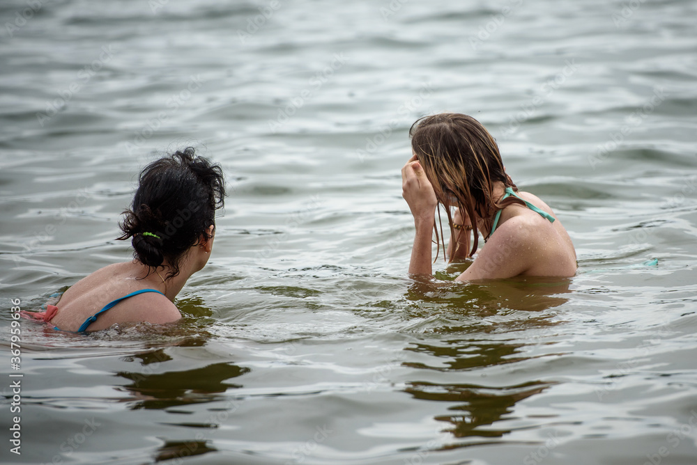 Fototapeta premium Two girls swim in the lake in the summer. The concept of a summer vacation.