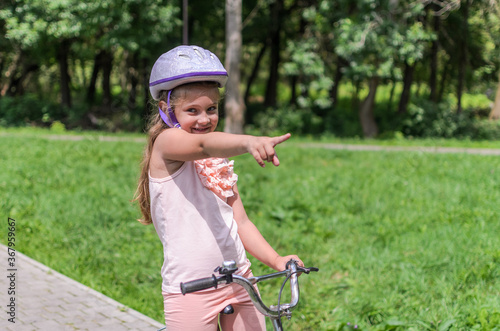 Little charming girl in a bicycle helmet rides a bicycle in the park 