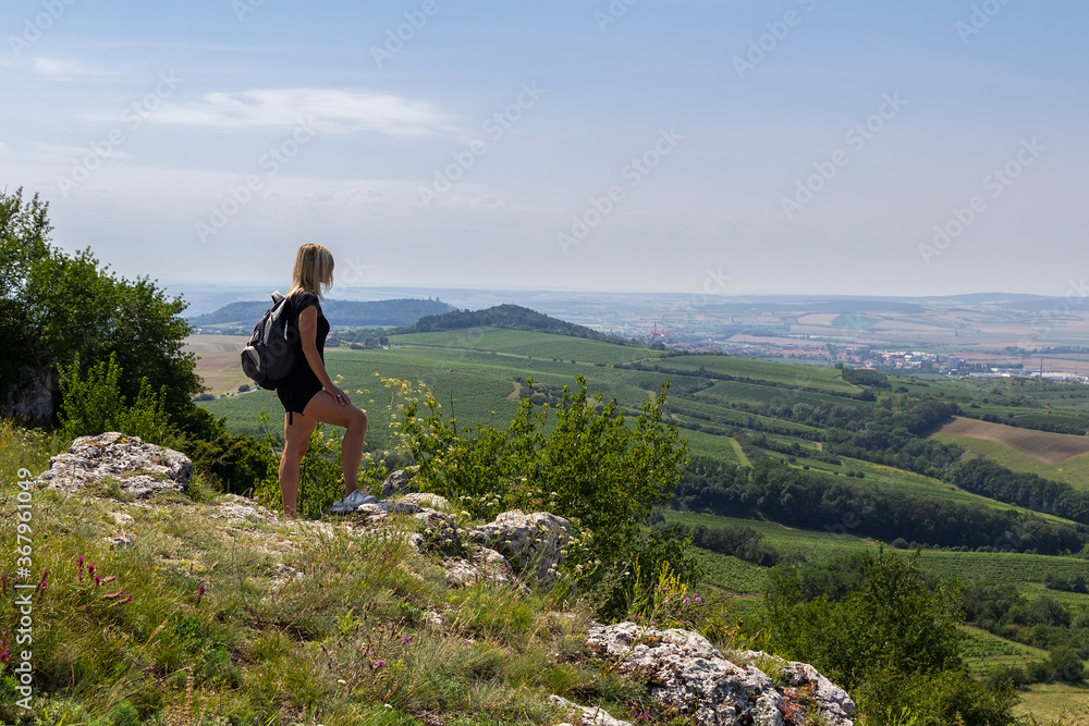 Young woman with backpack standing on lookout in black dress. Palava, Czech republic