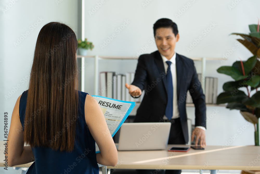 Young Asian executives in a black suit Smiling, welcoming the young woman candidate to submit a resume for applying a job Young Asian executives in a black suit Smiling, welcoming the young woman candidate to submit a resume for applying a job