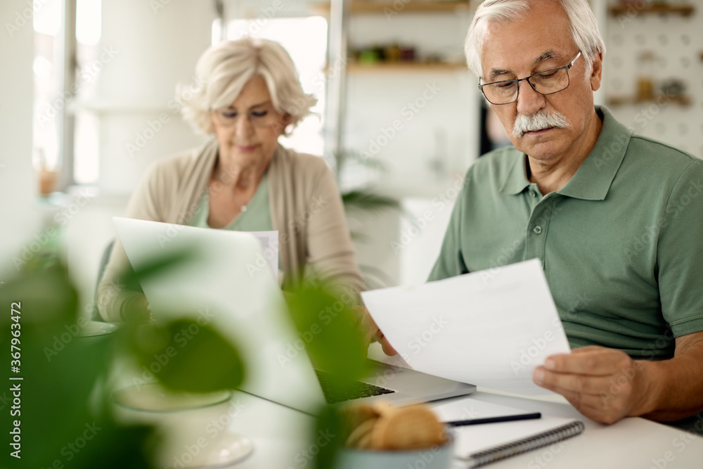 Mature couple analyzing their financial bills while paying them online at home.