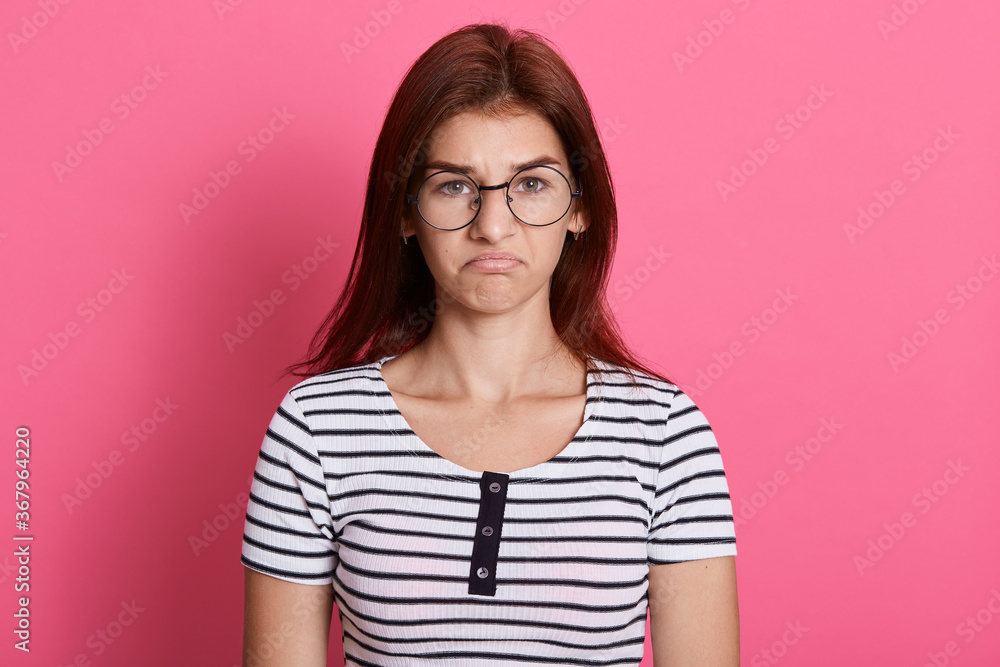 Portrait of disappointed cute girl wearing striped casual t shirt looking directly at camera with upset facial expression, posing isolated over pink background. Portrait of disappointed cute girl wearing striped casual t shirt looking directly at camera with upset facial expression, posing isolated over pink background.
