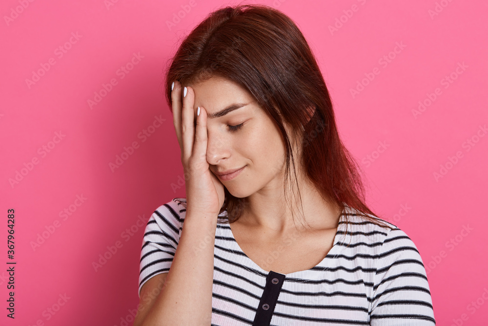Tired young woman covers face with palm, closes her eyes, feels exhausted, wearing casual striped t shirt, posing isolated over pink background, wants to sleep. Tired young woman covers face with palm, closes her eyes, feels exhausted, wearing casual striped t shirt, posing isolated over pink background, wants to sleep.