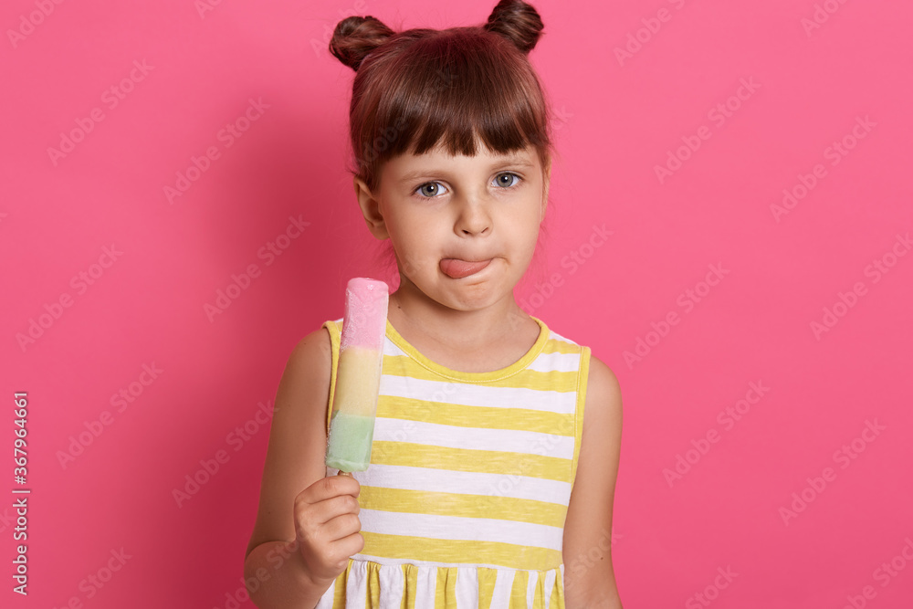 Funny little girl looking directly at camera while licking her lips, charming female child enjoying eating fruit sorbet, posing isolated over rosy background. Funny little girl looking directly at camera while licking her lips, charming female child enjoying eating fruit sorbet, posing isolated over rosy background.