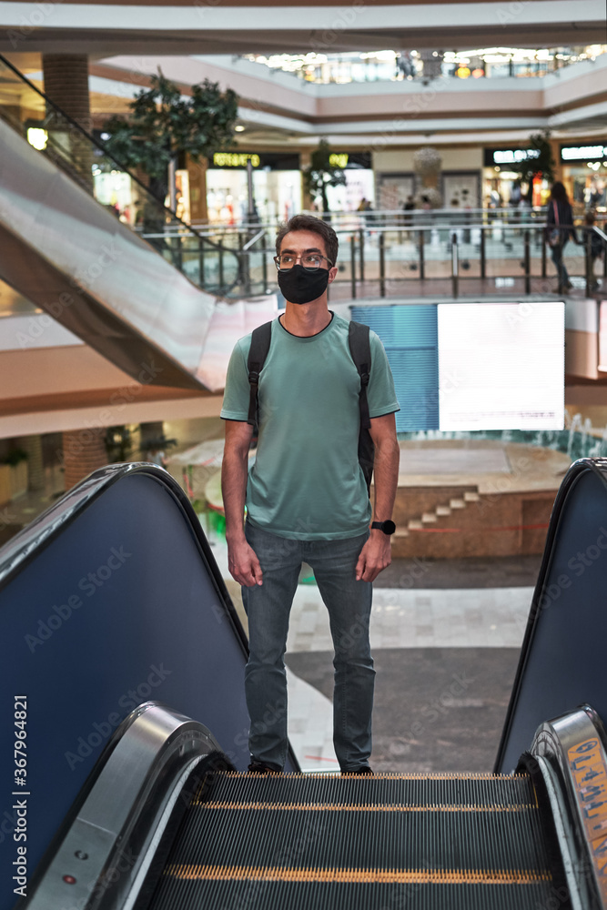 Young man in a protective mask standing on an escalator in a shopping center