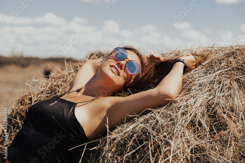 Beautiful young girl with long hair in sunnglasses posing on a wheat field near hay bales. photo