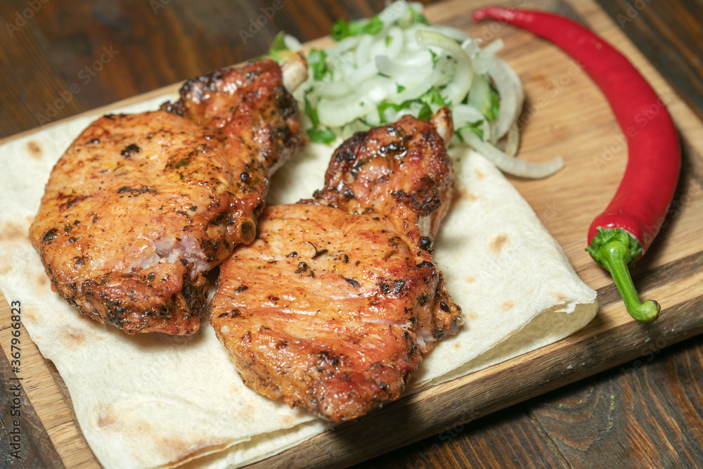 Spicy hot grilled spare ribs from a summer BBQ served with a hot chili pepper and fresh tomatoes on an old vintage wooden cutting board.