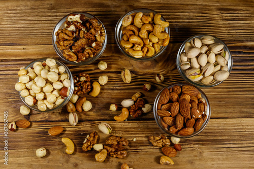 Assortment of nuts on wooden table. Almond, hazelnut, pistachio, walnut and cashew in glass bowls. Top view. Healthy eating concept