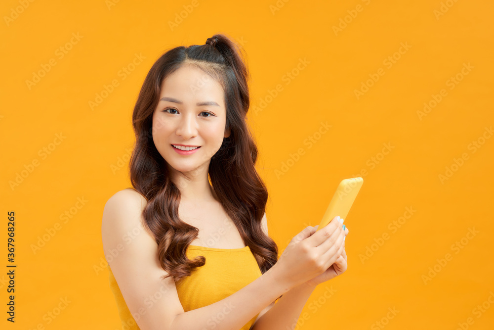 Attractive young Asian woman using phone over orange background. Attractive young Asian woman using phone over orange background.