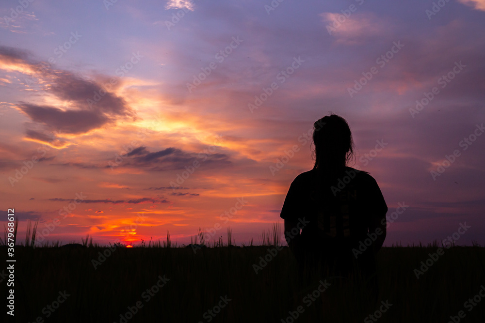 Silhouette of a woman standing on a field and looking at a beautiful sunset and colorful sky