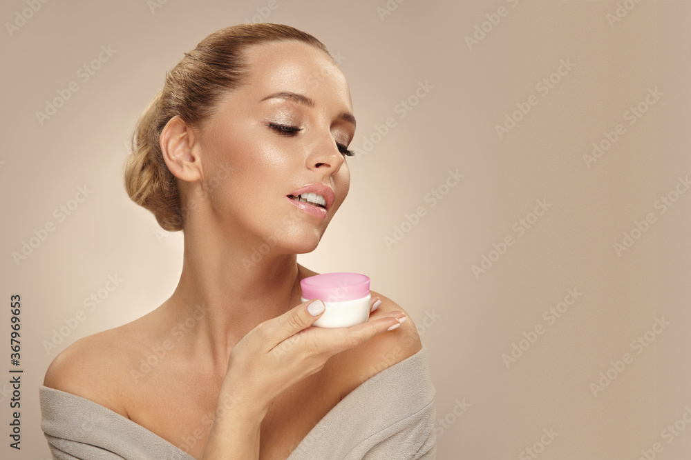 Female beauty model looking away, holds near her face natural eco safety cream on beige isolated, close up portrait with free copy space. Female beauty model looking away, holds near her face natural eco safety cream on beige isolated, close up portrait with free copy space.