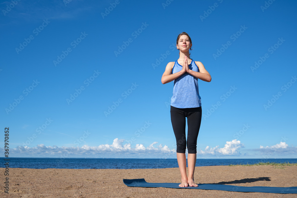Young slim girl doing yoga on the beach on a sunny morning, sun salutation stand, stretching before doing sports Young slim girl doing yoga on the beach on a sunny morning, sun salutation stand, stretching before doing sports