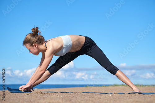 Young slim girl doing yoga on the beach on a sunny morning, stretching before doing sports