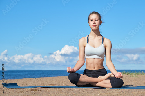 Young slim girl doing yoga  lotus position on the beach  relaxation and meditation