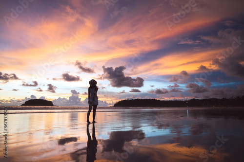 Rear view of young adult tourist asian woman walking relax on beach sand with beautiful dramatic sunset sky