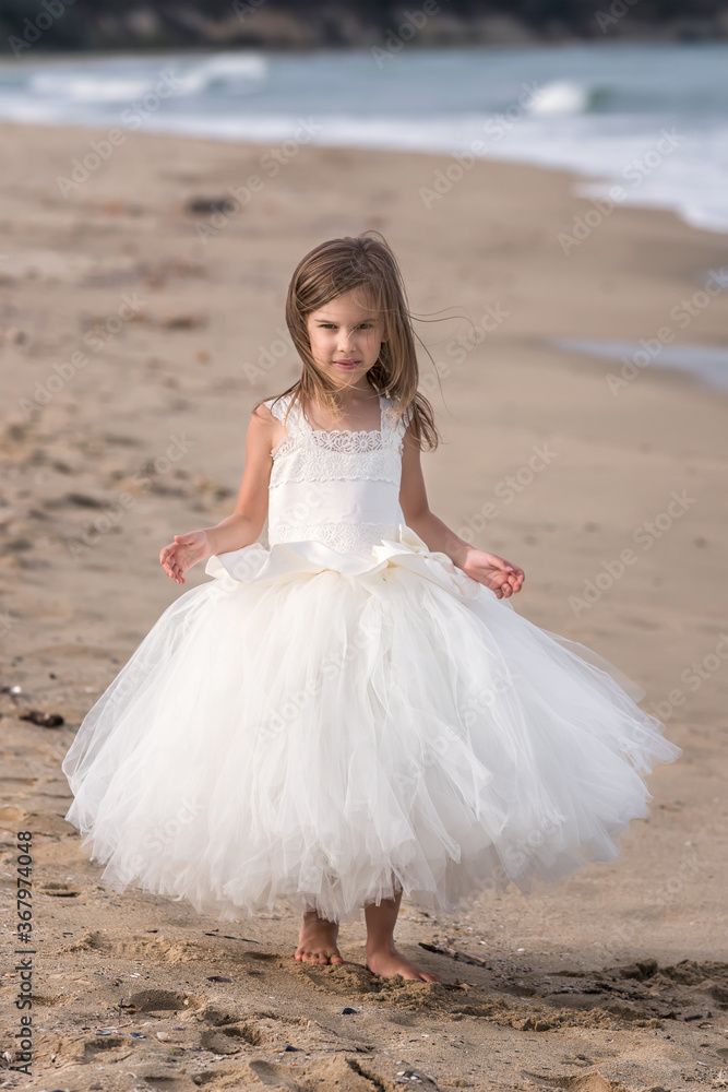 Dance on the beach.A beautiful little girl in a white ballet dress walks and dances on a sandy beach