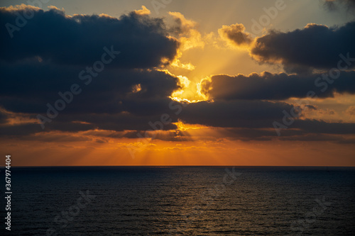 Beautiful sunset with golden colors over the sea with clouds covering/hiding the sun, the sunbeam and sun rays are coming out from the clouds 