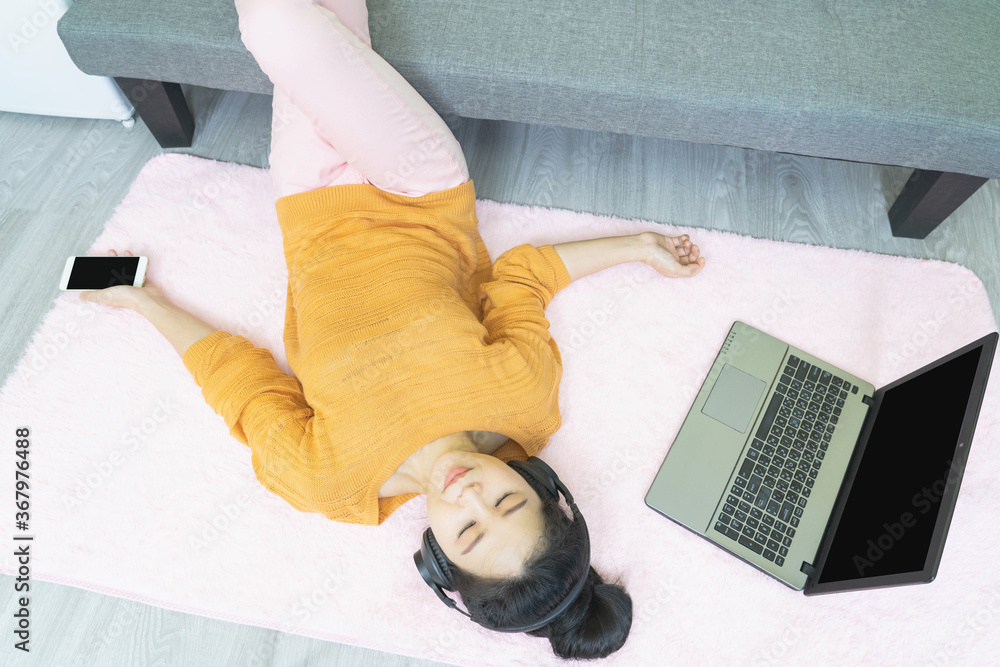 people and leisure concept - happy young asian woman in headphones lying on pink carpet with laptop,