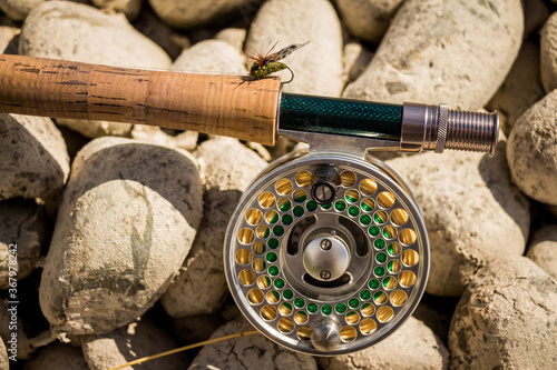 A close up of a trout fly rod, reel and line on rocks, with a cicada fly photo