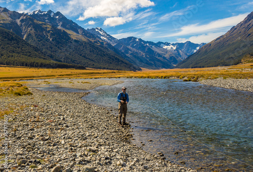 An Angler fly fishing for trout on the Ahuriri river, surrounded by mountains, New Zealand © Jozef