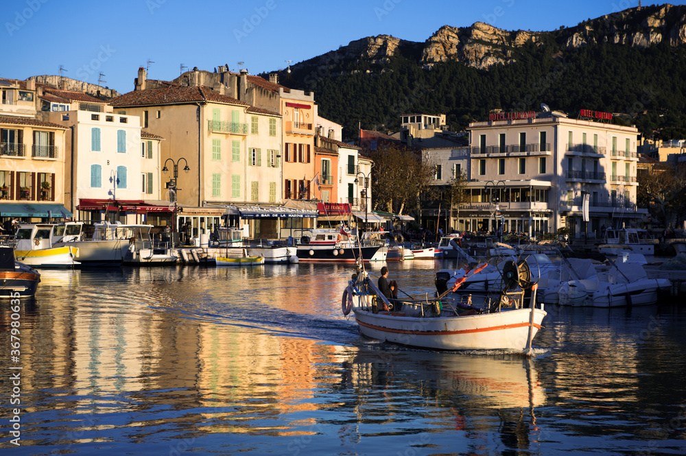 Fisher boat leaving tranquil harbor of ancient Cassis in France in sunset.