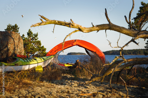 Orange tent, yellow kayak on the island. Kayaking, camping equipment, outdoor activities. Tent in focus, background blurred.