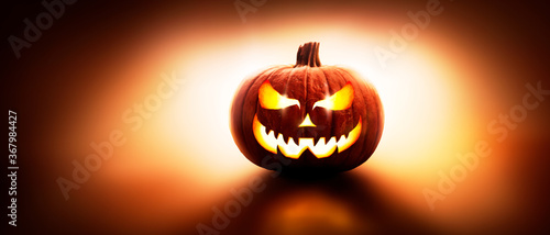 A back lit halloween lantern, Jack o Lantern, with a spooky evil face with glowing eyes against a dark background. photo