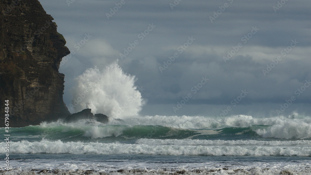 Powerful waves breaking and crashing on rocks, at Piha Beach, Auckland, NZ