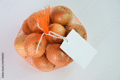 Onions in net bag with white tag isolated on gray