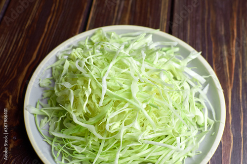 Chopped fresh green cabbage salad on ceramic plate on wooden table background.