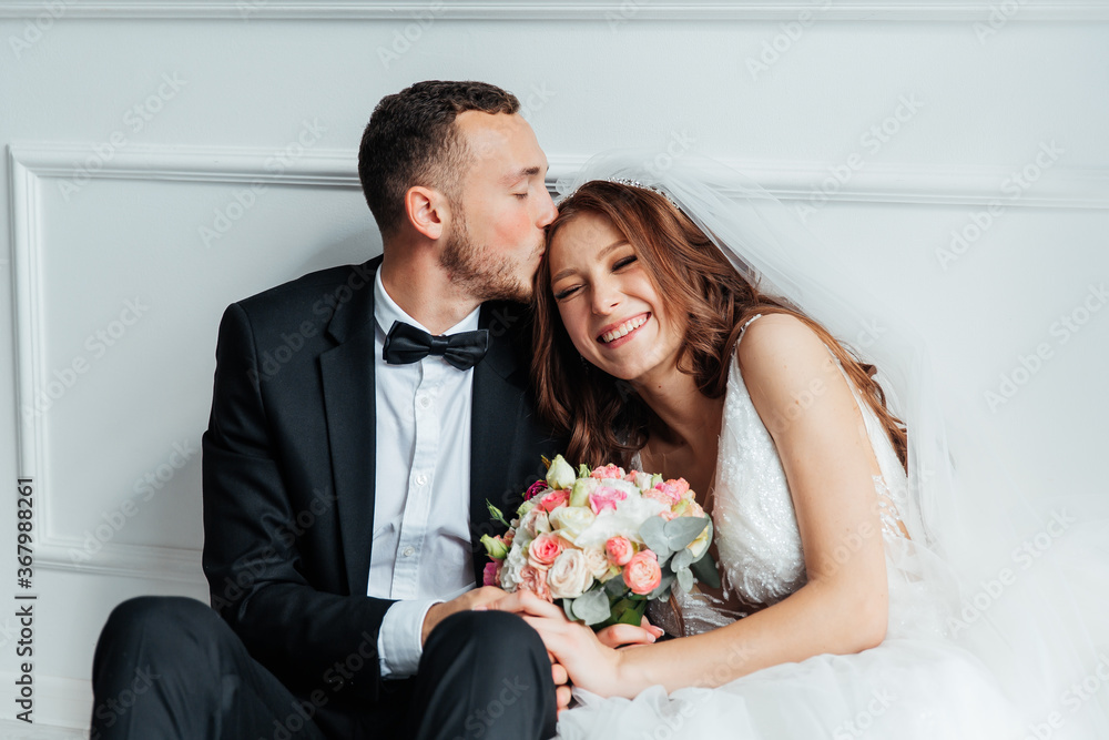 The first meeting of the groom in a black suit and the bride in a white wedding dress with a bouquet in the interior of a photo studio on a white and black background The first meeting of the groom in a black suit and the bride in a white wedding dress with a bouquet in the interior of a photo studio on a white and black background
