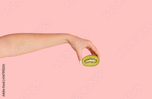 Female hand holding cut kiwi fruit against pink background, closeup