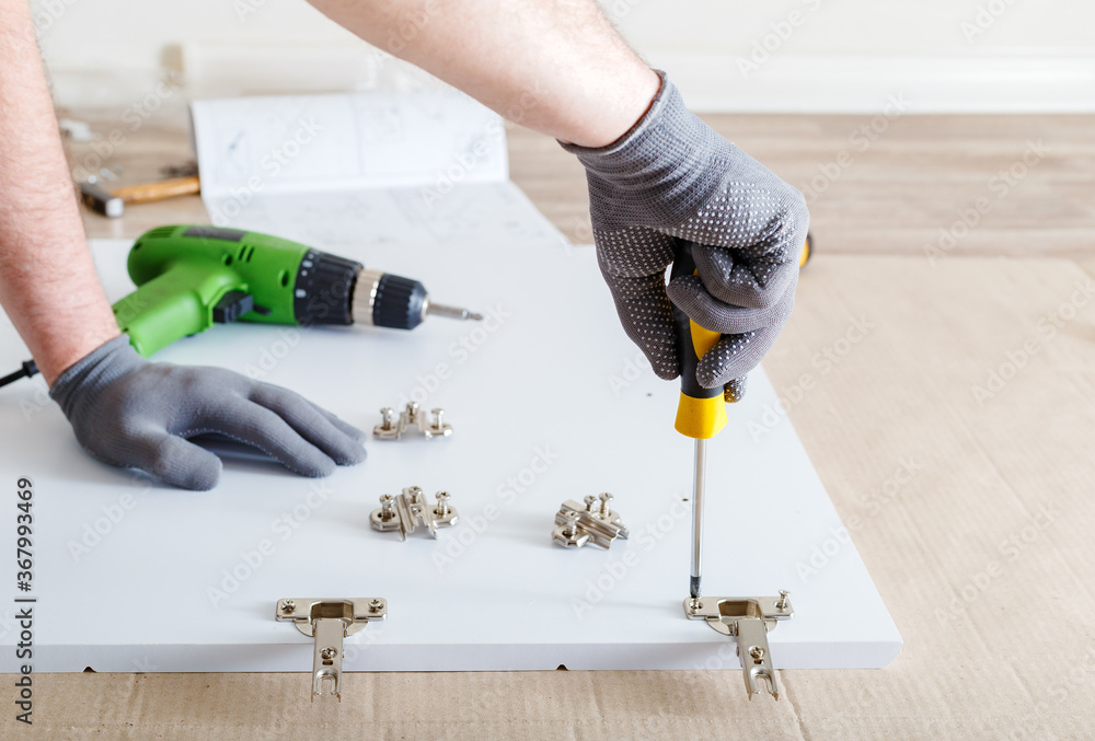 Furniture assembly using screwdriver. Male hands in gray gloves master collects furniture using screwdriver tools, instrument at home. Moving, home improvement, furniture repair and renovation