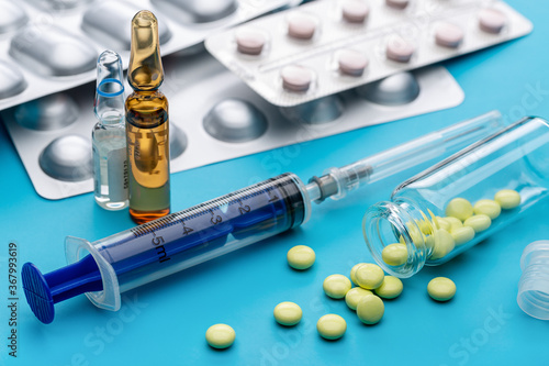 Syringe for injection and ampoule with the drug. In blisters, tablets for treatment. Blue background. Health care concept.