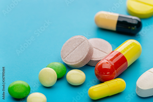 Colorful assortment of pills and capsules on  blue background, close-up.