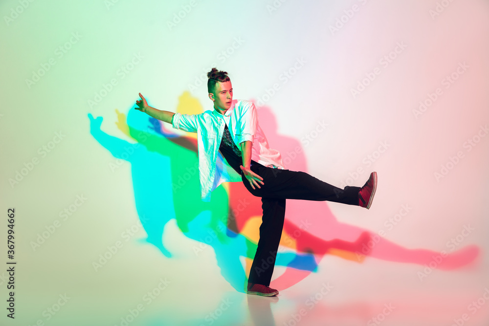 Young beautiful man dancing hip-hop, street style isolated on studio background in colorful neon light. Fashion and motion, youth, music, action concept. Trendy clothes. Copyspace for ad.