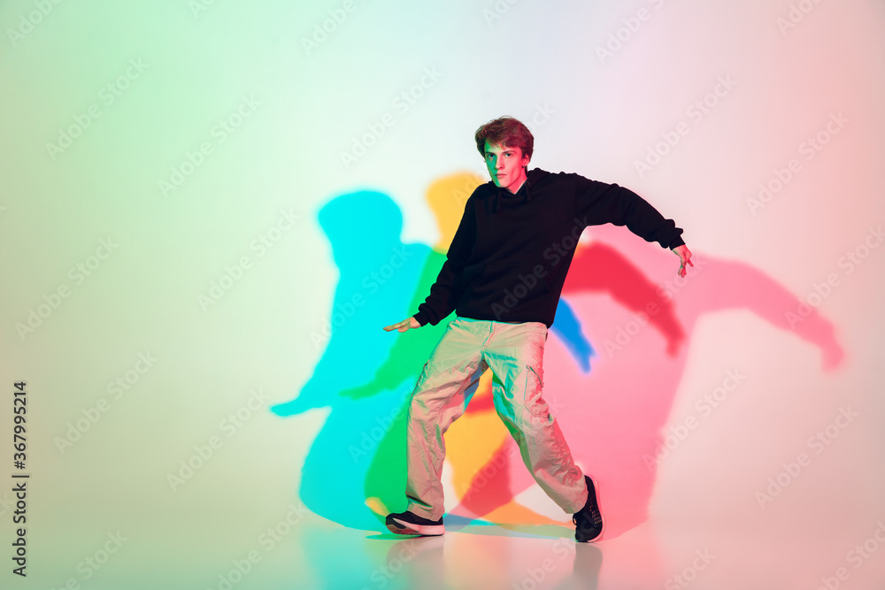 Young beautiful man dancing hip-hop, street style isolated on studio background in colorful neon light. Fashion and motion, youth, music, action concept. Trendy clothes. Copyspace for ad.