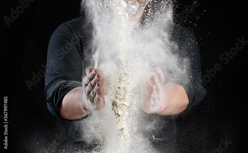 chef in black uniform sprinkles white wheat flour in different directions, product scatters dust © nndanko