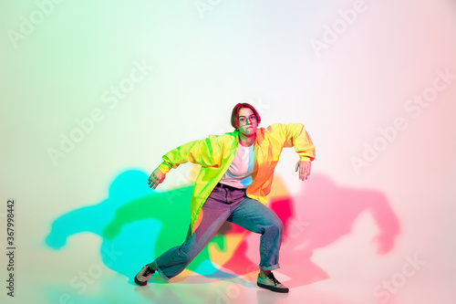 Young beautiful woman dancing hip-hop, street style isolated on studio background in colorful neon light. Fashion and motion, youth, music, action concept. Trendy clothes. Copyspace for ad.