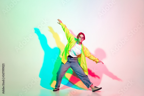 Young beautiful woman dancing hip-hop, street style isolated on studio background in colorful neon light. Fashion and motion, youth, music, action concept. Trendy clothes. Copyspace for ad.