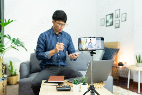 Young asian male blogger recording vlog video on camera review of product at home office, Focus on tripod mounted camera screen broadcast live stream video to a social network.